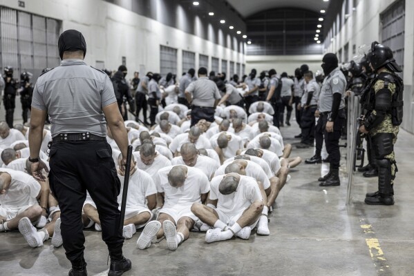 In this photo provided by El Salvador's presidential press office, a prison guard transfers deportees from the U.S., alleged to be Venezuelan gang members, to the Terrorism Confinement Center in Tecoluca, El Salvador, Sunday, March 16, 2025. (El Salvador presidential press office via AP)